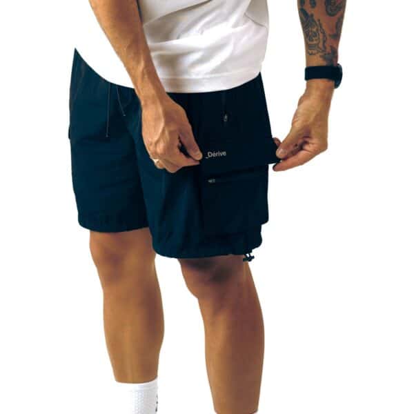 Dérive DRFT black cargo shorts, model opening the zipped side pocket