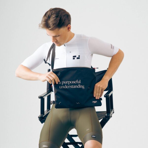 Seated rider opening the black Dérive Purposeful Musette to reach essentials