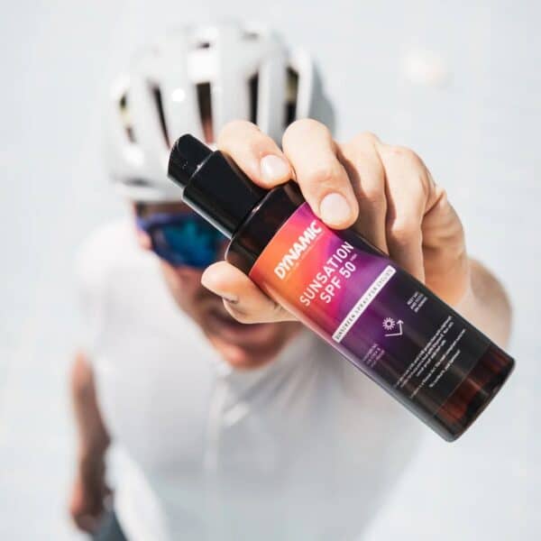Cyclist holding up a 200 ml bottle of Dynamic Sunsation SPF 50 sunscreen spray