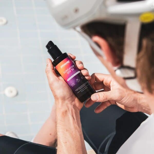 Cyclist holding a bottle of Dynamic Sunsation SPF 50 sunscreen spray before applying it
