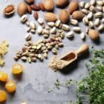 Ingredients of the Veloforte Zenzero bar laid out on a stone surface: almonds, pistachios, candied fruit and spices